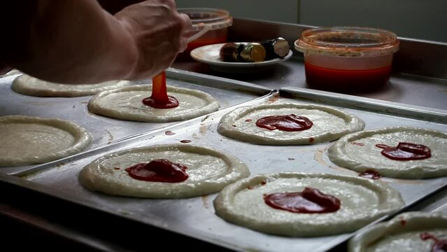 Pizza maker smears sauce on pizza dough pieces. The chef prepares pizza in a restaurant or pizzeria.