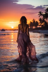 Seductive blonde woman in sexy dress posing on the beach in sunset light. Perfect wavy hairs, tan skim body. Summer tropical mood. View from back.