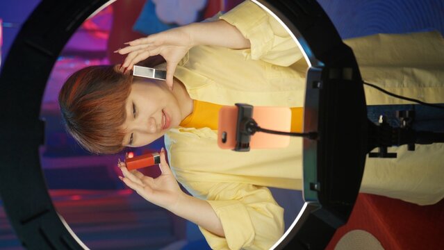 Beautiful girl in casual clothing demonstrating a different lipsticks in front of the camera at home studio. Vertical photo