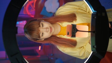 Beautiful girl blogger in casual clothing and shiny hair standing in front of the smartphone.