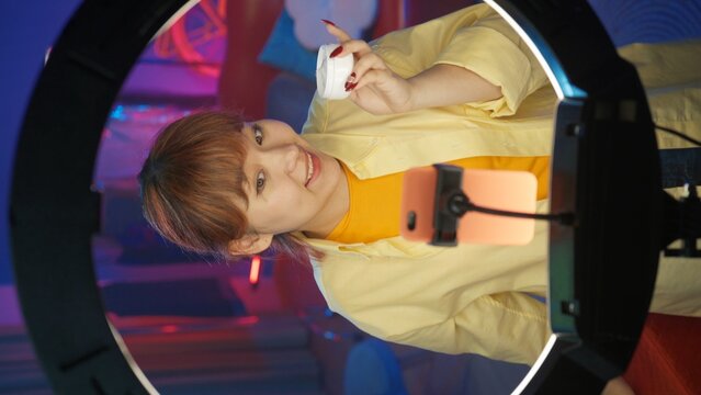 Attractive girl blogger in casual clothing holding a jar of face cream in front of the camera. Vertical photo