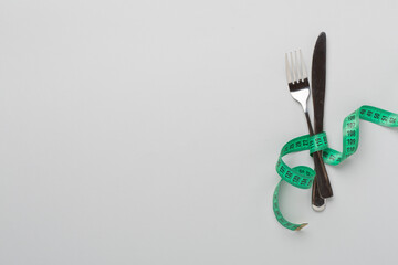 Knife and fork wrapped in tape measure on color background, top view