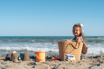 beautiful little brunette girl 4 years old is played in the sand on the seashore in a white dress