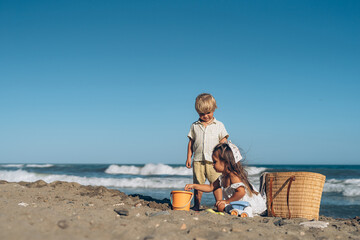 a little boy and a girl of three years old play in the sand on the beach near the sea