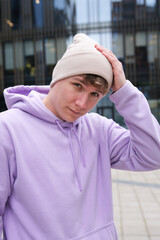 Portrait of young happy man or teenager in hoodie and hat looking at camera outdoors