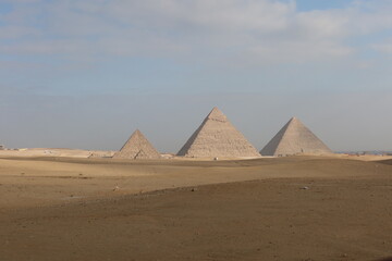 The three pyramids of Egypt side by side in the middle of desert sand with the sky in the background