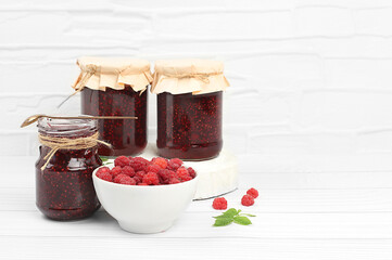 Village harvest, jars of raspberry jam on light wooden background with leaves, shop banner and advertisement, healthy natural food concept, breakfast with ingredients, home canning concept,