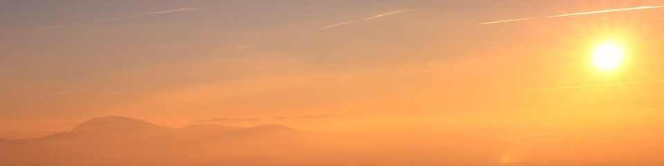 Naklejka na ściany i meble Banner sunset over mountains, yellow sun in cloudy haze