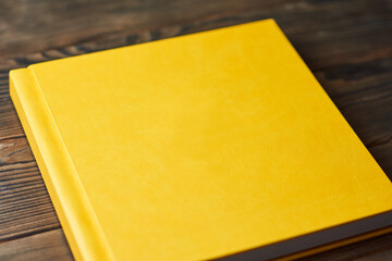 Photo album with bright yellow hardcover isolated on a brown wooden background. Perspective view,...