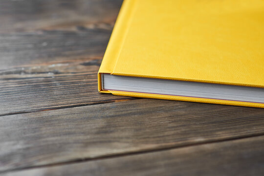 A cropped image of thick book with yellow textured hardcover isolated on a wooden desktop with copy space for text. Template for photographers or designers.
