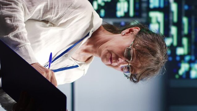 Vertical video Knowledgeable serviceman in data center equipped to handle complex computational operations, doing regular upgrades to server units, increasing processing power to prevent hazards