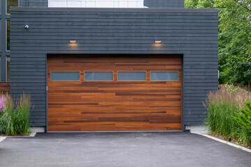 A modern brown faux wooden exterior garage door with four small horizontal glass windows. The...