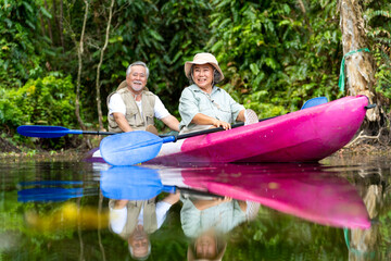 Asian senior couple kayaking together in the lake at mangrove forest on summer vacation. Retired...