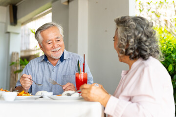 Happy Asian family senior couple having lunch and sharing meal together at restaurant. Elderly people man and woman enjoy retirement with outdoor activity lifestyle on summer holiday travel vacation.
