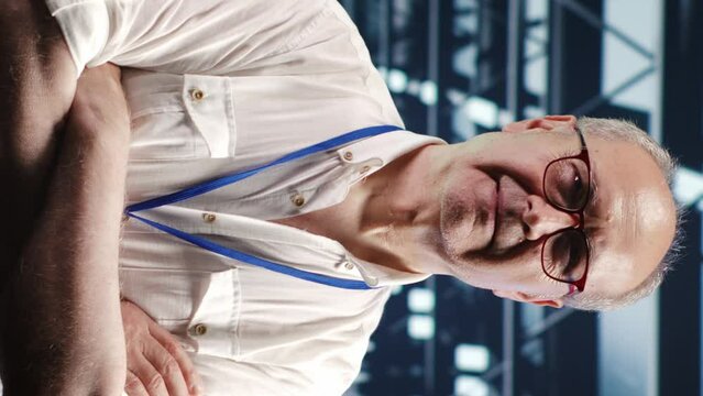Vertical video Portrait of senior technician looking around modern server hub in data center, preparing to start comission on malfunctioning high tech workplace hardware racks in order to ensure