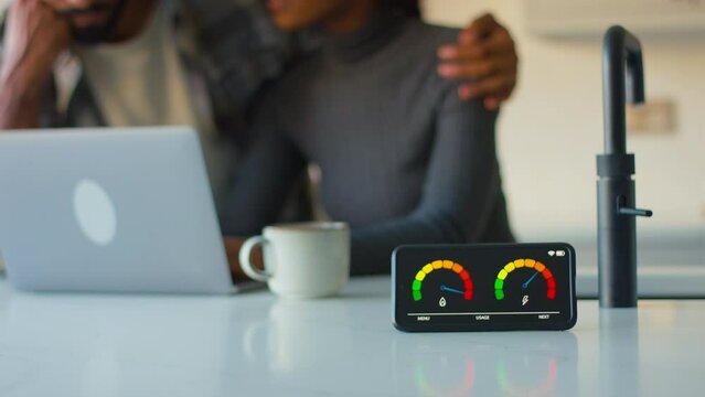 Couple at home in kitchen with energy meter looking at laptop concerned about cost of living crisis - shot in slow motion