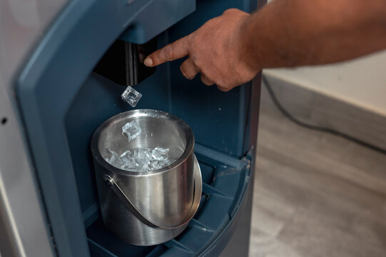 A man presses down on a lever to drop ice cubes from a dispenser into a small stainless bucket. Using a commercial grade hotel ice maker.