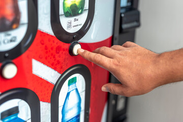 A man selects a beverage from a cold soda vending machine. Pressing a button to get the drink of...
