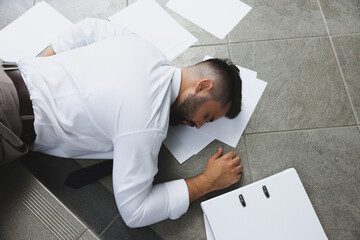 Unconscious man with scattered folder and papers lying on floor after falling down stairs indoors,...