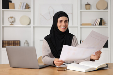 Muslim woman working near laptop at wooden table in room