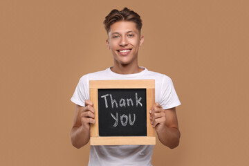 Happy man holding small chalkboard with phrase Thank You on brown background
