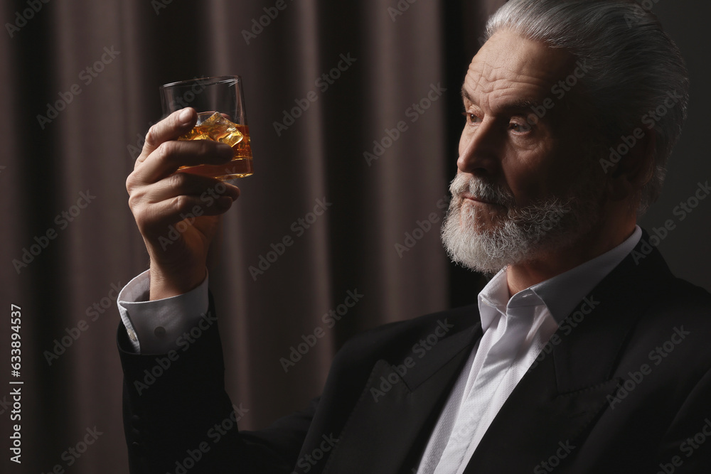 Poster Senior man in formal suit holding glass of whiskey with ice cubes on brown background