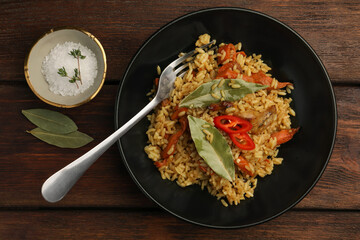 Delicious pilaf, bay leaves, fork and salt on wooden table, flat lay