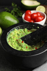 Mortar with delicious guacamole and ingredients on table