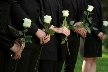 People in black clothes with white rose flowers outdoors, closeup. Funeral ceremony