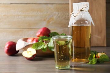 Delicious cider and apples with green leaves on wooden table, space for text