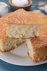 Plate with cut tasty sponge cake on light blue wooden table, closeup