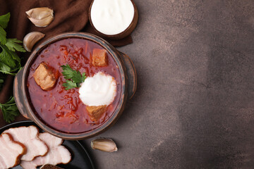 Tasty borscht with sour cream in bowl served on brown textured table, flat lay. Space for text