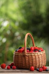 Wicker basket with different fresh ripe berries on wooden table outdoors