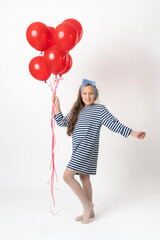 Girl holding large bunch of red balloons in hand, looking at camera. Full length studio shot of model 10 years old in white blue striped dress standing on white background. Part of photo series