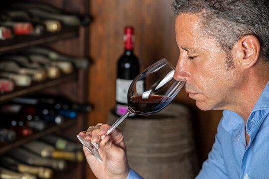 SOMMELIER SMELLING A RED WINE GLASS IN A WINE TASTING AT A WINERY.