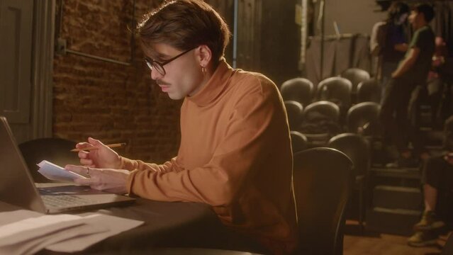 Professional playwright typing on laptop and making notes on papers while working on theater stage. Medium handheld shot