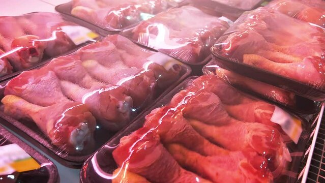 Chilled chicken leg quarters packaged in food grade plastic containers covered with cling-wrap in a supermarket fridge. Close-up shot