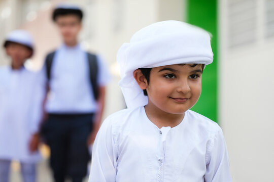 Arab student at school with classmates on the background wearing traditional Kandura Dish dasha for Emirati, Saudi, Qatar, Oman, Kuwait or Bahrain education concept. Happy Arabic boy.