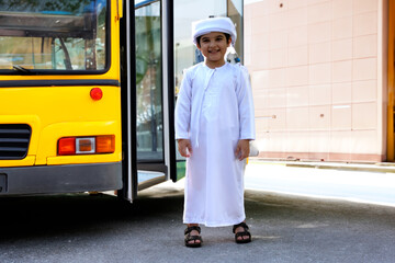 Full body standing shot of Arabic boy near a school bus ideal for education diversity concept....