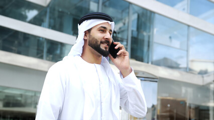 Standing Full body of Arab Middle Eastern Gulf Man at a business centre using mobile cellphone calling concept. Arabic Emirati businessman on call using smartphone
