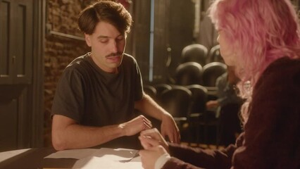 Angry male actor sitting at table on theater stage, quarreling with female partner, playing couple in argument during rehearsal or drama performance. Over the shoulder shot
