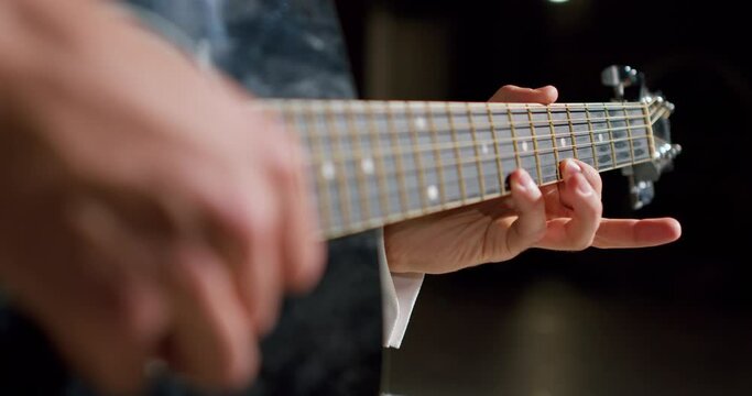 man in blue shirt strikes chords on acoustic classical guitar in theater hall Dark background Rehearsal in black room Closeup cropped slow motion Guy improvises on instrument, fingers holding mediator