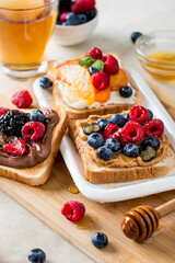 A plate of toast with cream cheese, peanut and chocolate paste with raspberries, blueberries, peaches, sprinkled with honey. Morning breakfast..