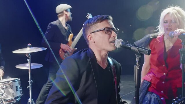 Band playing rock music on stage. Male and female singers are singing with artists. Performers performing together in concert.