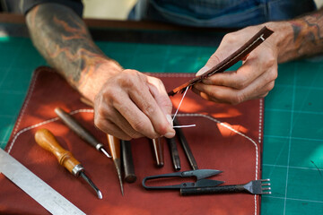 Closeup and crop hands of leather craftsman sewing a leather brown bag for a customer.