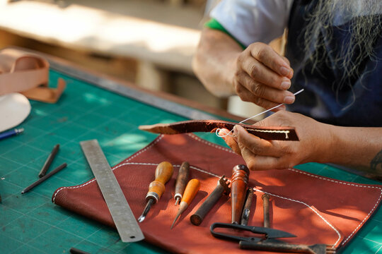 Closeup and crop hands of leather craftsman is working hard to sew a leather product for a customer.