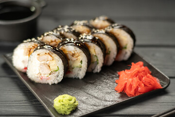 Futomaki with fried tuna, salmon and cream cheese served on stone plate over black wooden background