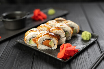 Roll with fresh raw salmon, smoked eel, cream cheese and avocado on black wooden background