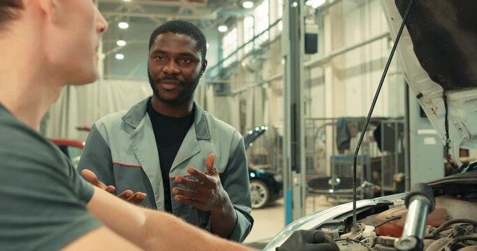 two colleagues talking having conversation about broken car, discussing repair process . mechanics sharing experience, African American man giving advise to caucasian guy Slow motion