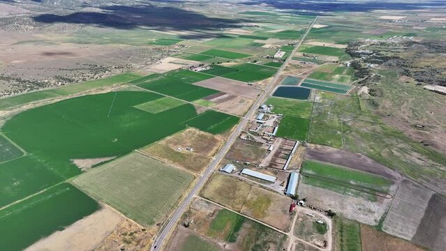 Aerial rural town traffic valley agriculture fields Utah 2. Farming community agricultural economy. Spring summer weather mountain valley green agriculture field. Homes, barns and buildings.
